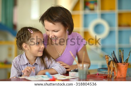 Little girl painting with her nice mother