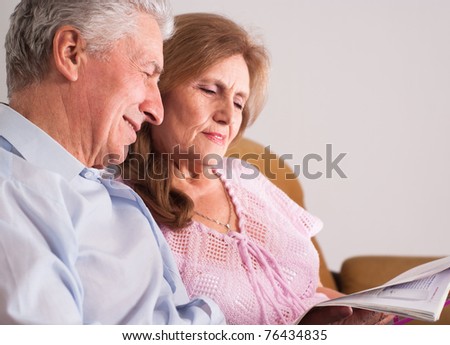 happy elderly couple reading a magazine on sofa
