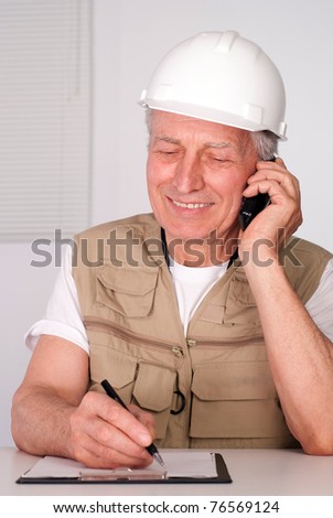 senior builder sitting and writing with phone