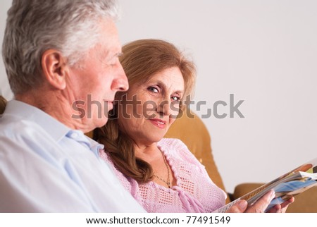 happy elderly couple reading a magazine on sofa