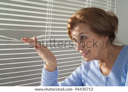 An elderly woman looks out the window on a light background