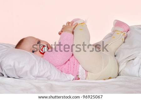 Little girl with a charming pacifier lying on the bed and keeps himself in the leg