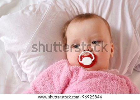Little girl with a charming pacifier lying on the bed