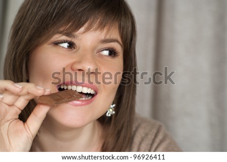 Luck smiling beautiful woman holding a chocolate bar on a gray background