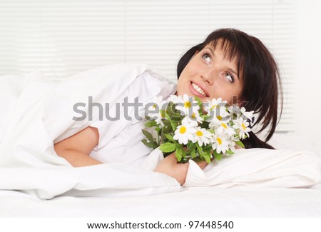Beautiful charming girl lying in bed with a bouquet of daisies
