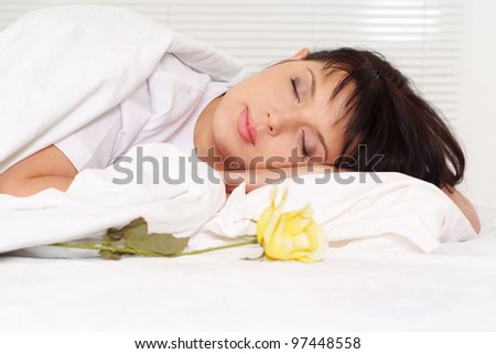 Beautiful charming girl sleeping on a bed near the pillow is a flower