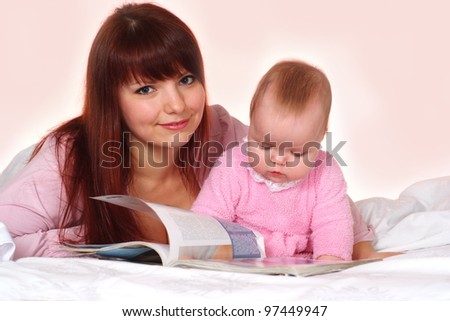 Beautiful charming mother and daughter lying in bed on a pink background