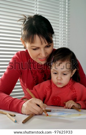A beautiful Caucasian mama and daughter holding pencils on a light background