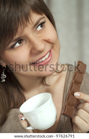 Smiling charming beautiful woman holds in one hand and a cup of chocolate in the other