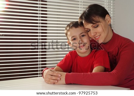 A beautiful caucasian luck mother hugs her son sitting at a table on a light background