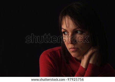Beautiful sad caucasian woman in red sitting on a black background