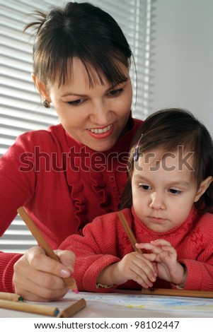 A beautiful Caucasian mom and daughter holding pencils on a light background