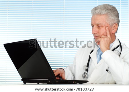 Happy Caucasian doctor with a computer sitting on a light background