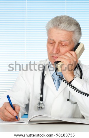 Happy Caucasian doctor with a telephone sitting on a light background