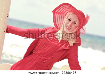 Fashion shot of blond young woman in red dress ,sea background, tuscany