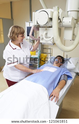radiographer aligning X Ray machine onto chest of teenage boy in radiology department