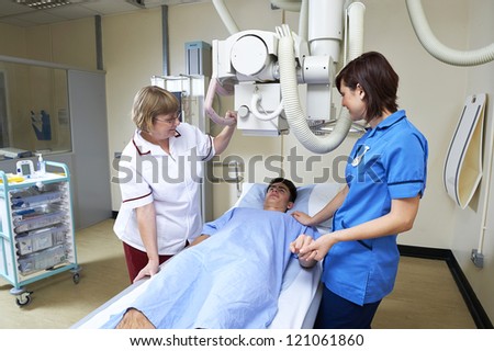 radiographer aligning X Ray machine over teenage male patient, while nurse reassures him