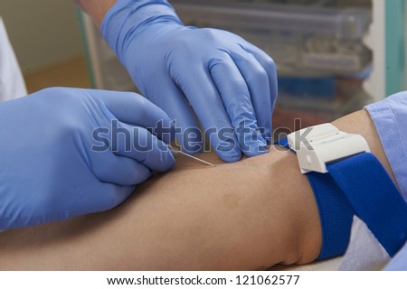 clinitian wearing blue medical gloves preparing to insert a cannula into a patients arm showing medical trolley in background