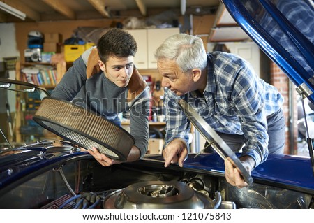 father and son working together on a classic car in a garage with air filter cover open looking in