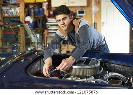 teenage boy leaning over the engine of a classic car in garage holding wrench