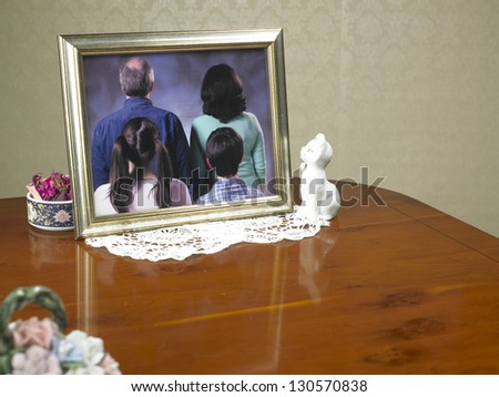 family portrait photograph with the family turned away from the viewer on a wooden table surface and ornaments to suggest an old person\'s house