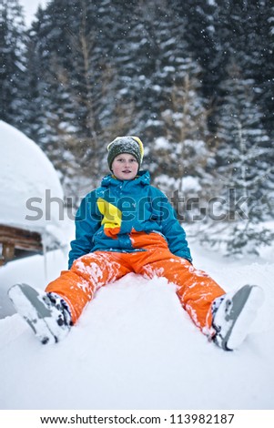 Picture of a young smiling boy sitting in a pile of snow. Trees in the background