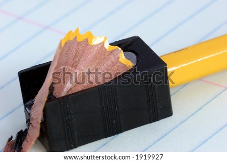 Yellow pencil being sharpened in a cheap black sharpener, on blue lined school notebook paper.