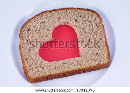 Red heart pattern cut in a slice of whole grain bread, on a white plate.