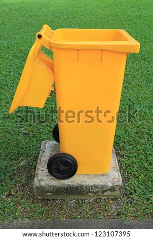 Large yellow trash can on green grass field background