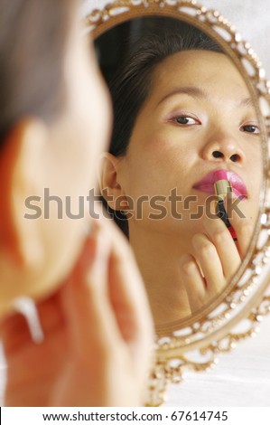 woman looking into mirror for applying lipstick on lips