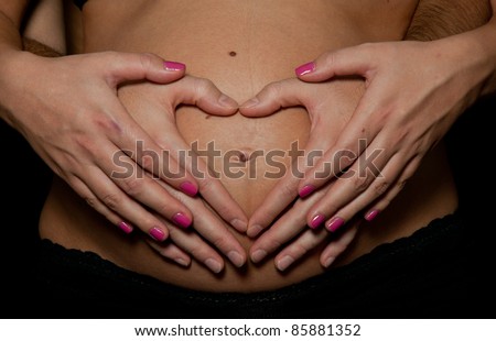 Pregnant woman making heart shape with hands over her stomach isolated over black background