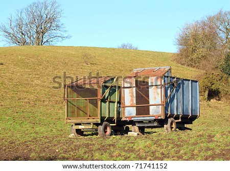 Two rusty abandoned farm trailers in field with blue sky