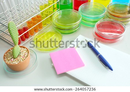 note book on laboratory table with Colorful fluid in  glass ware