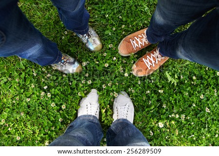 Group of friends standing in a circle on a spring meadow but only their feet in sneakers is visible