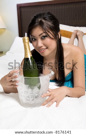 Pretty Asian woman on bed with wine glass and Champagne bucket