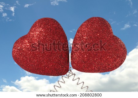 Two Glittery Red Hearts on Cloudy Blue Sky Background