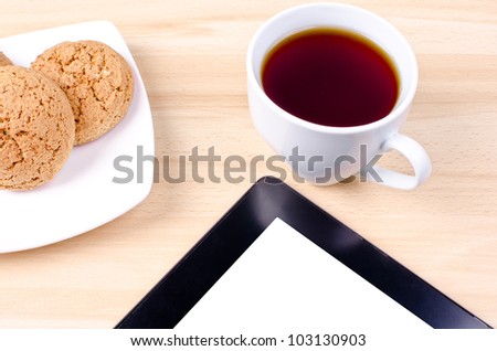 Blank digital black tablet on a desk with empty white screen and cup of coffee and plate with cookies