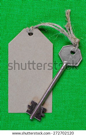grey paper tag attached to the metal silver key on the green  fabric background