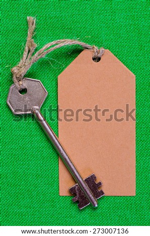 brown paper tag attached to the metal silver key on the green  fabric background