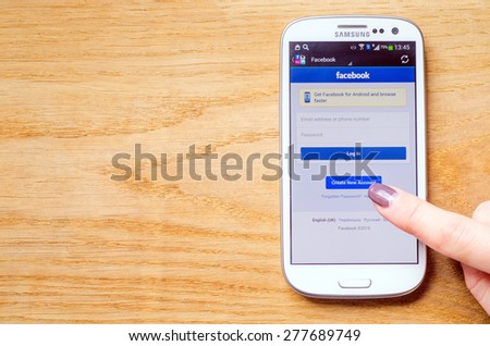 LVIV, UKRAINE - May 03, 2015: Hand holding white Samsung Smart Phone with Facebook Social Network Log In Screen, and women try create new account, on wooden background