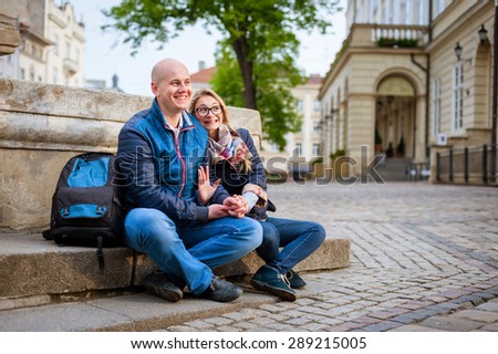 Young fashion elegant stylish couple, travel by old European cities, sitting on an old stone, with a backpack, on the square with paving stones