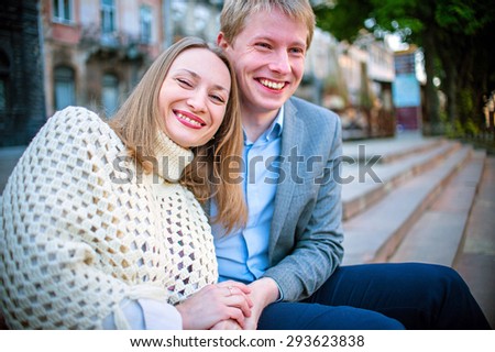 Young fashion elegant stylish couple, travel by old European cities, sitting on an old stone, with a backpack, on the square with paving stones, smiling