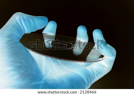 This is an image of a hand hold a data cd in a (dark technology room) lab like environment