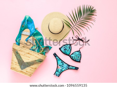 Bikini swimsuit with tropical print, silver glitter flat sandans, straw hat, wicker beach bag, sarong, tropical palm leaves on pink background. Overhead view of woman\'s swimwear and beach accessories.
