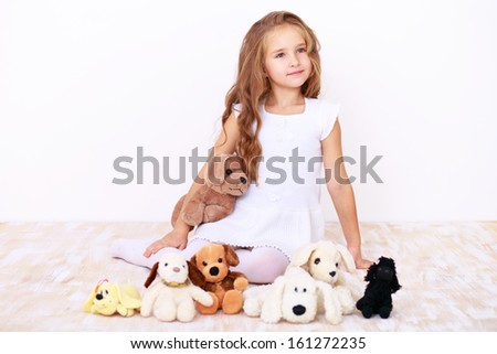 Cute blonde little girl in white dress sitting on the floor with her teddy dogs