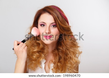 Beautiful woman with makeup brush near her face on grey background