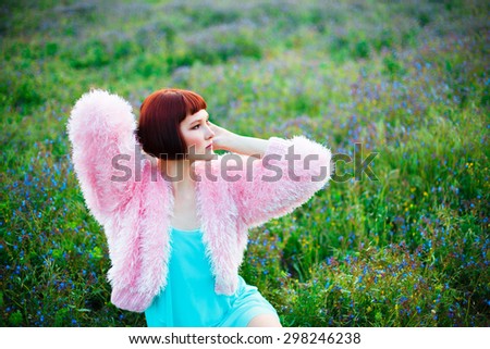 Beautiful woman in a pink fur coat sitting among a field of wild flowers