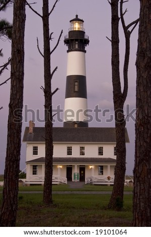 A front view of the Bodie Island Lighthouse and Museum at dusk framed in southern pines.