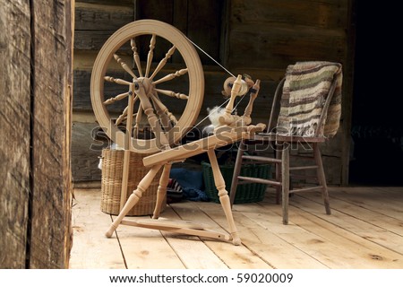 A spinning wheel with yarn baskets and old chair on a log cabin porch.