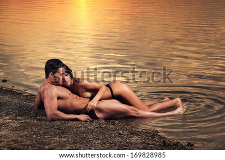 Young sexy couple on beach with sun rising in background .Fashion colors.